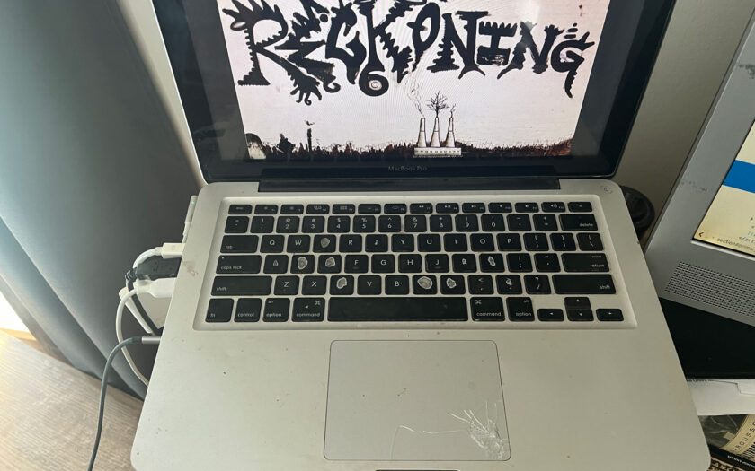 My early 2011 MacBook Pro in all its ragged glory, featuring worn keys, spiderweb-cracked touchpad, and Steve Logan's Reckoning 1 artwork of a smokestack sprouting a tree.